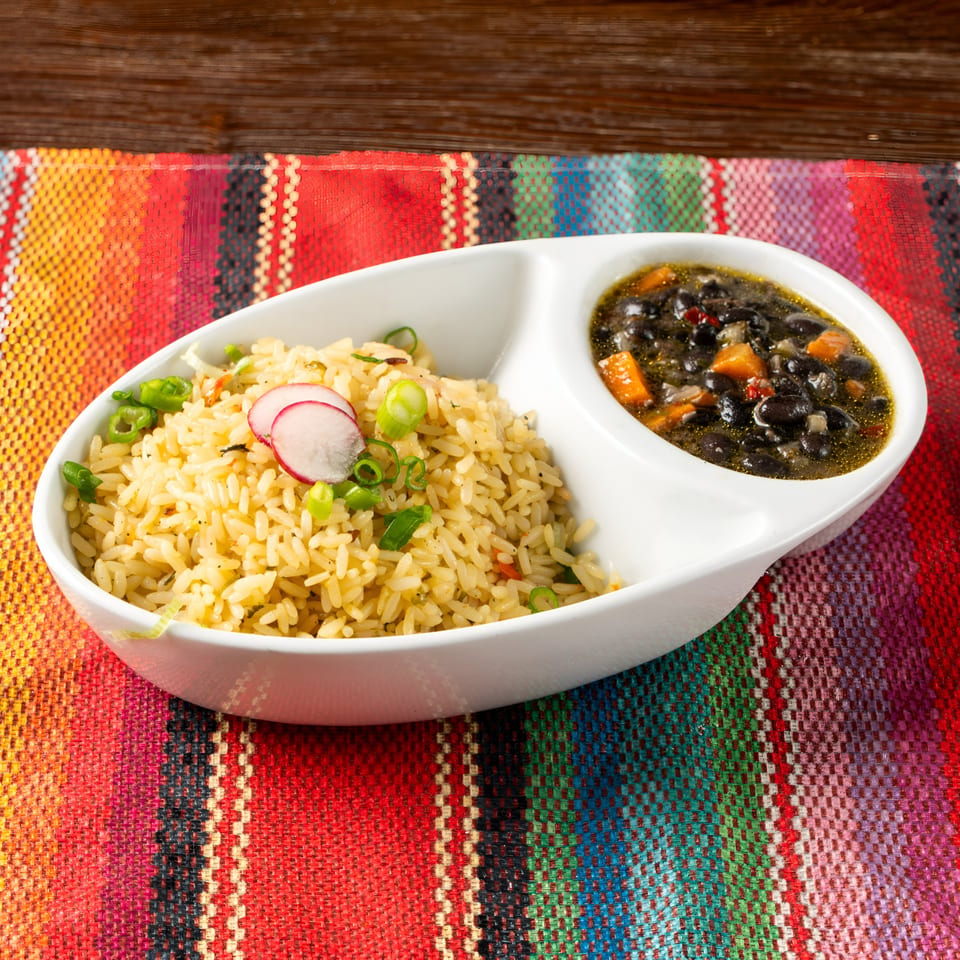 Mexican rice with radishes and black bean soup in a white divided bowl on a colorful placemat.