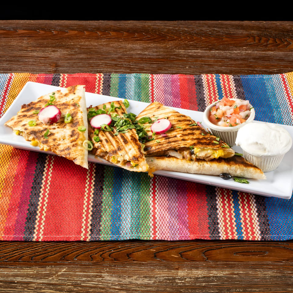 Grilled quesadillas with radishes, green onions, salsa, and sour cream on a colorful striped placemat.